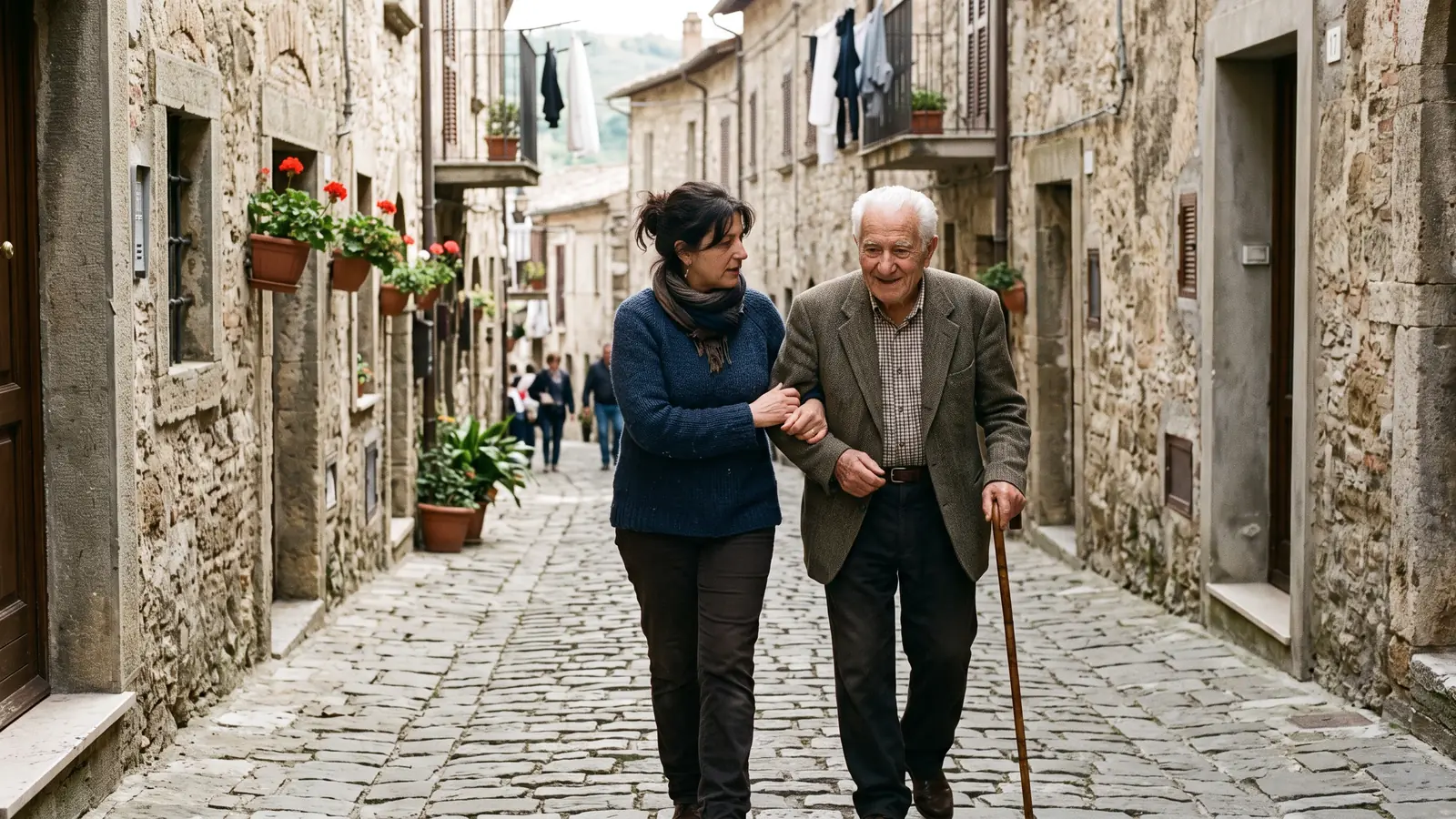 Una donna accompagna sottobraccio il padre anziano con il bastone in una strada del centro storico.